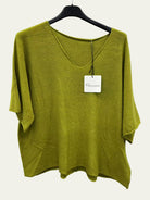 An olive green short-sleeve knit top with a V-neck, hanging on a black hanger against a white wall. 