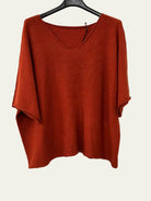 A burnt orange-red knit top with a wide V-neck and elbow-length sleeves