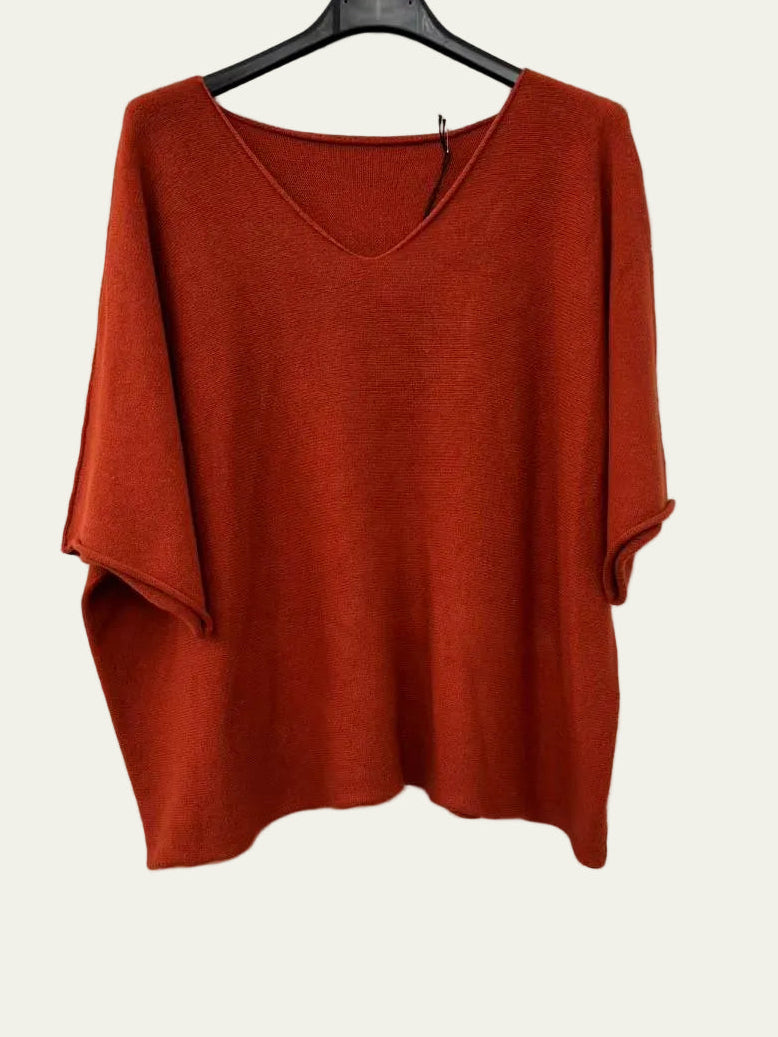 A burnt orange-red knit top with a wide V-neck and elbow-length sleeves