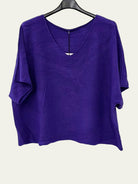 A purple short-sleeve V-neck top hanging on a black hanger against a plain white wall.