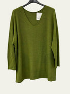 An olive green long-sleeve knit top with a V-neck, hanging on a black hanger against a white wall.