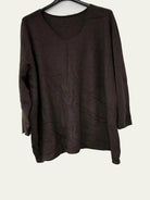 A dark brown long-sleeve knit top with a V-neck, hanging on a black hanger against a plain white wall.