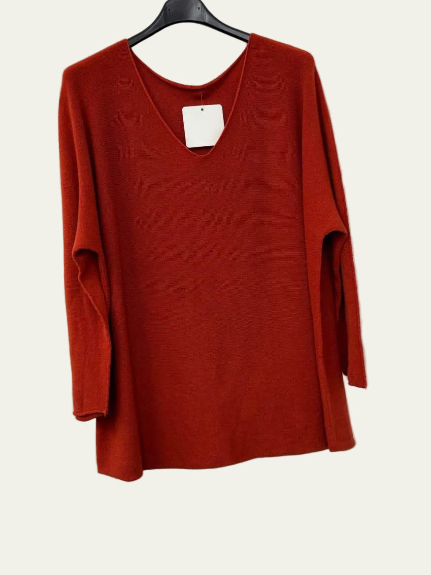 A rust red long-sleeve knit top hanging on a black hanger against a white wall.