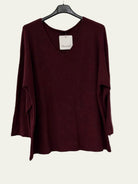 A long-sleeve knit top in deep burgundy hanging on a black hanger