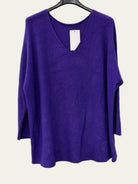 A purple knit long-sleeve top with a V-neck, hanging on a black hanger against a plain white wall.