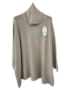 A beige knit turtleneck sweater with a ribbed mock neck collar, hanging on a white wall with a white product tag attached.