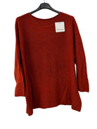 A rust-orange long-sleeve knit top hanging on a black hanger against a white wall, with a small white brand tag near the neckline.