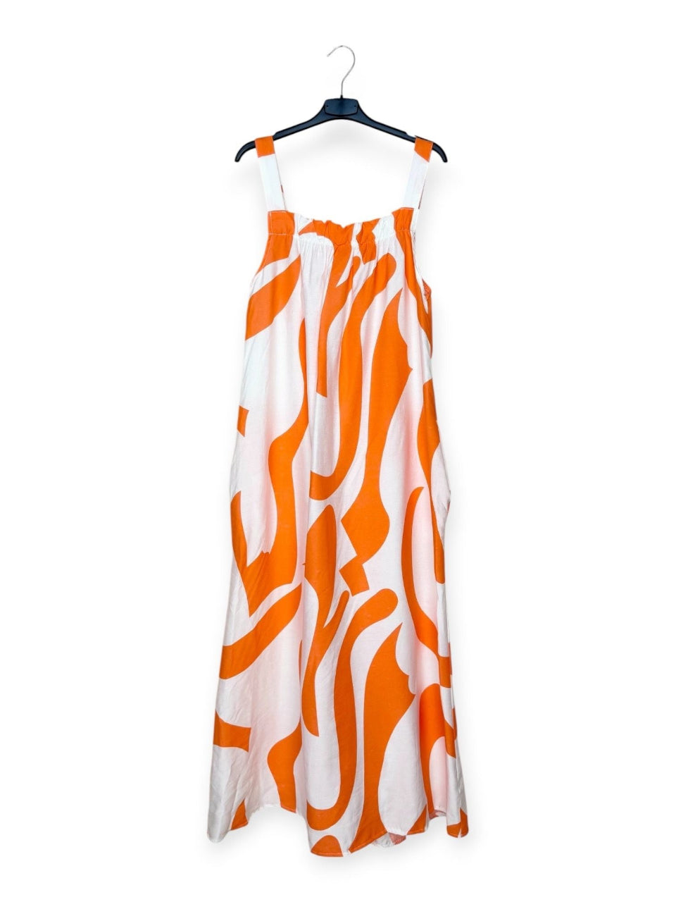 Orange and white patterned dress on a hanger against a white background