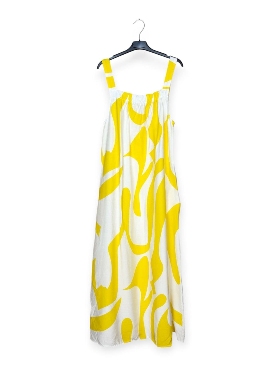 Yellow and white patterned dress on a hanger against a white background