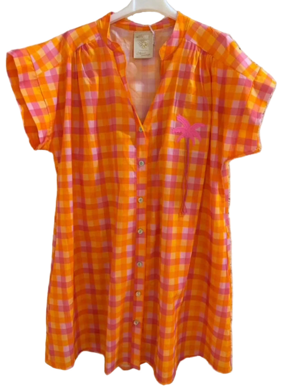 Orange and pink checkered shirt dress on a hanger against a textured wall.