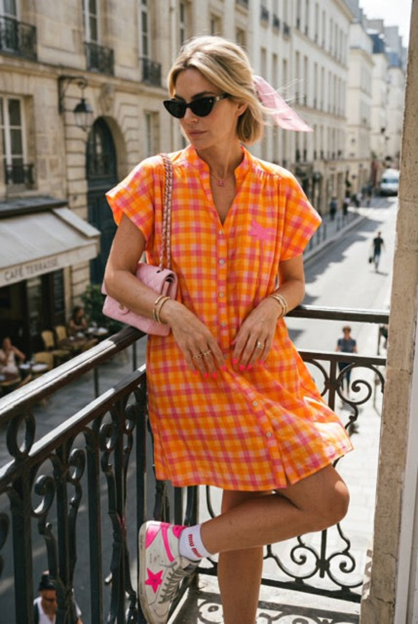 Woman in an orange checkered dress standing on a balcony in an urban setting