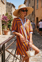 Woman in a colorful striped dress and sun hat walking down a street.