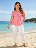 Woman in pink top and white pants standing on a beach with ocean and sky in the background