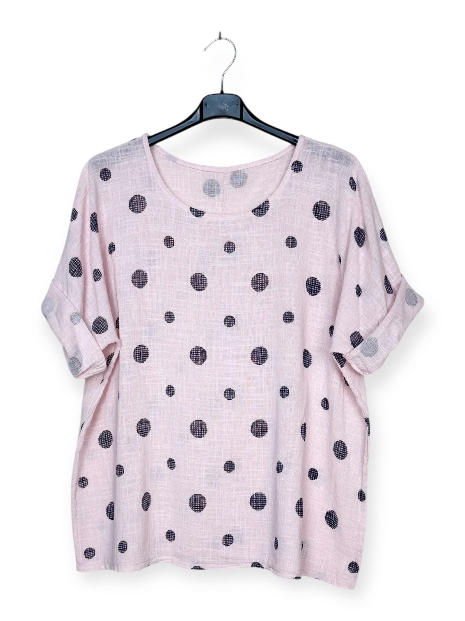 Pink top with black polka dots on a hanger against a white background