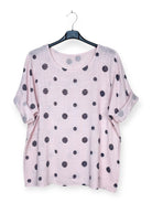Pink top with black polka dots on a hanger against a white background