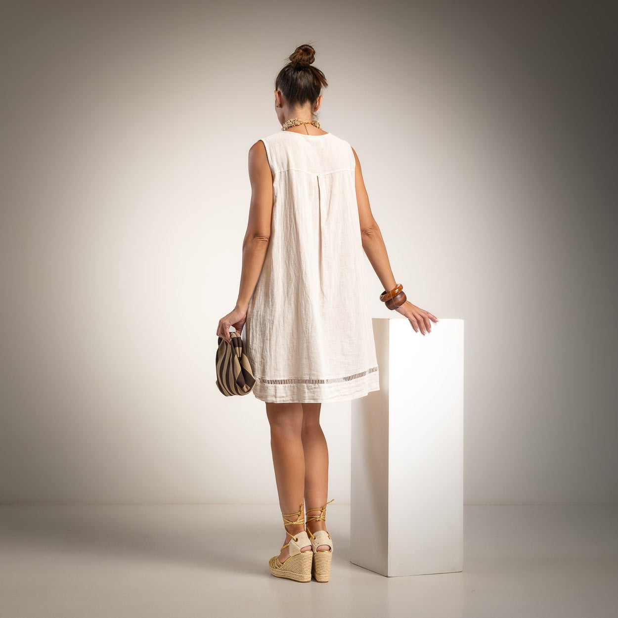 A woman stands with her back to the camera wearing a sleeveless beige dress with ladder detail