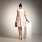 A woman stands with her back to the camera wearing a sleeveless beige dress with ladder detail