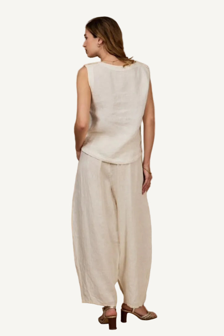 Woman wearing a beige sleeveless top and wide-leg pants against a beige background