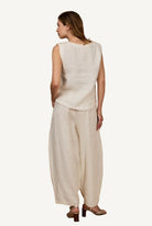Woman wearing a beige sleeveless top and wide-leg pants against a beige background