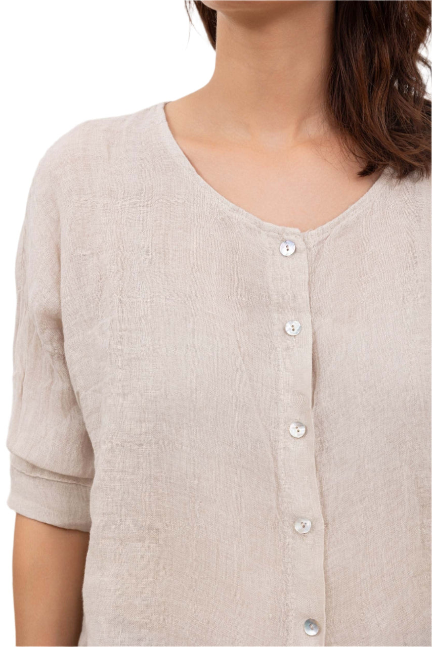 A woman wearing a beige one size pure linen button fronted collarless shirt with three quarter sleeves.