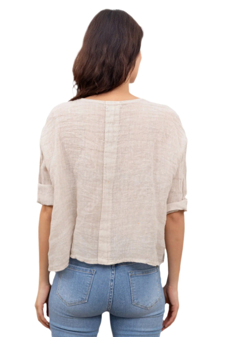 A woman wearing a beige one size pure linen button fronted collarless shirt with three quarter sleeves, paired with blue jeans.