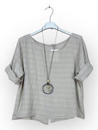 beige cotton top with a long necklace on a hanger against a white background