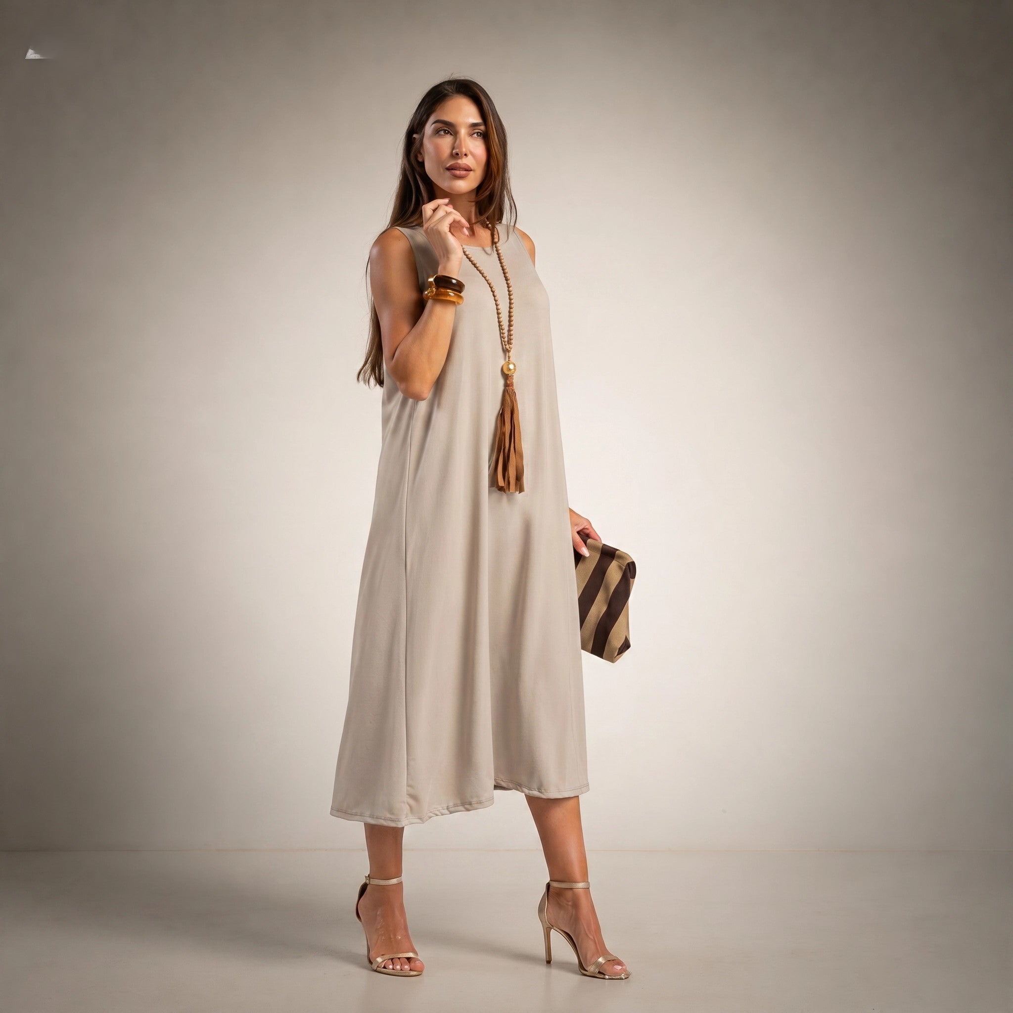 A woman models a sleeveless, midi-length beige dress with a relaxed, flowy silhouette. 
