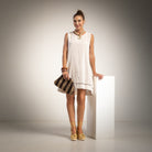 A woman stands in a studio wearing a sleeveless white mini dress