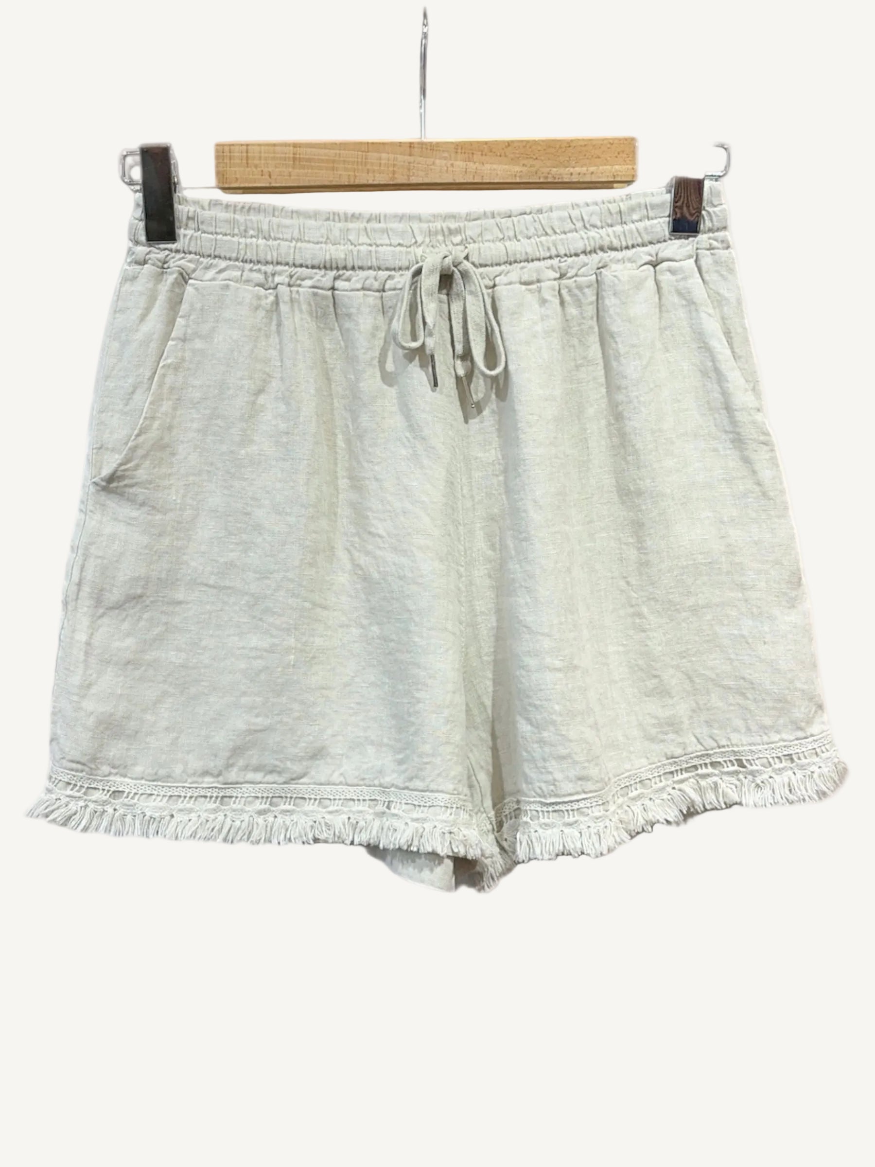Beige shorts with frayed edges on a hanger against a white background