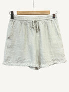 Beige shorts with frayed edges on a hanger against a white background
