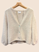 A soft knit cardigan sweater in beige, hanging on a wooden hanger - the cardigan features a V-neck, long sleeves, and a front button closure with light blue buttons.