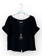 A black short-sleeve top with a wide scoop neckline, displayed on a white hanger with a long silver pendant necklace.