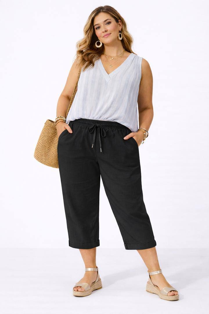 Woman wearing a white sleeveless top and black pants, standing against a white background.