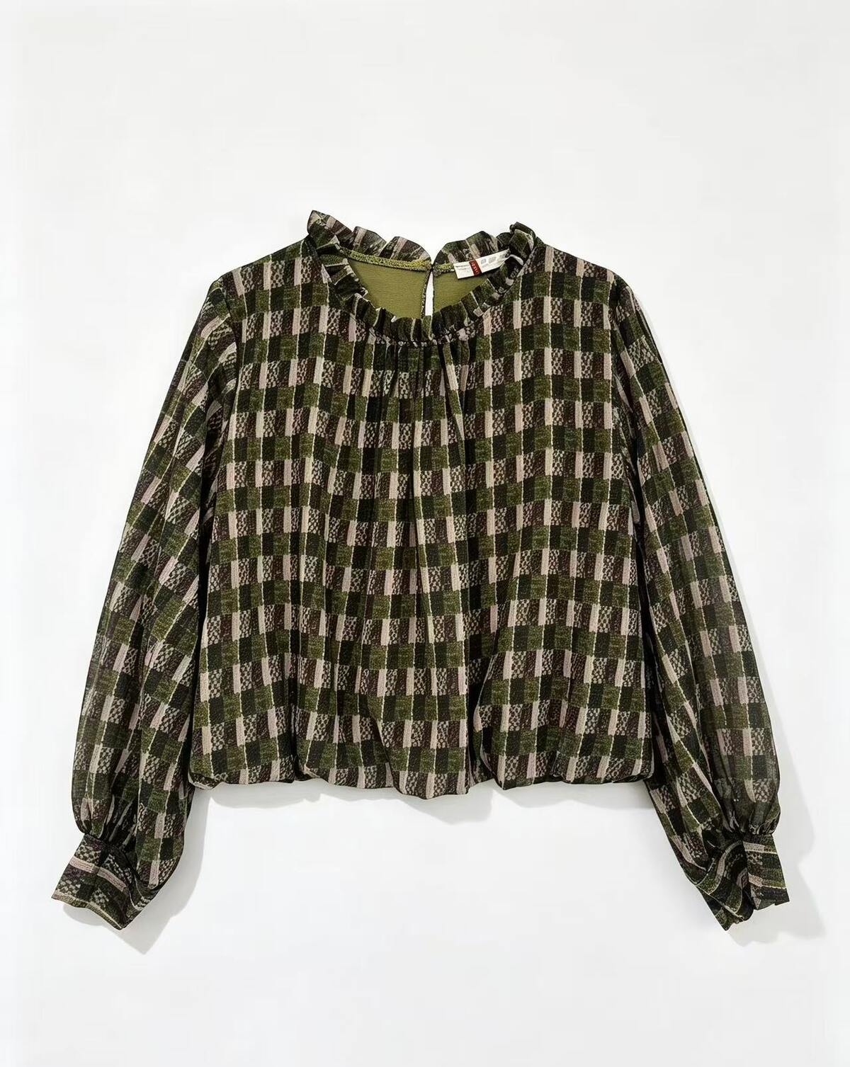 A long-sleeve blouse with a green, brown, and beige plaid pattern, featuring a ruffled high neckline and gathered cuffs, laid flat against a white background.