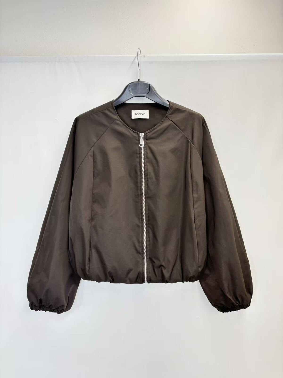 A dark brown zip-up jacket hanging on a black hanger against a plain white wall.