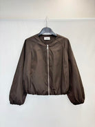 A dark brown zip-up jacket hanging on a black hanger against a plain white wall.