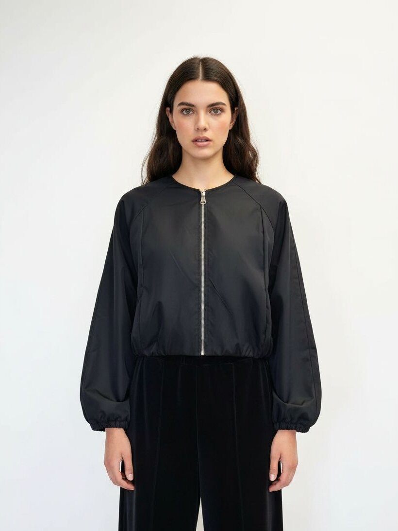 A woman modeling a black cropped bomber jacket with a silver front zipper and black wide-leg pants, shot against a plain white studio background.