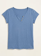 A short-sleeve henley t-shirt in a dusty medium blue color, featuring a three-button placket on a v-neckline, displayed flat against a light cream background.