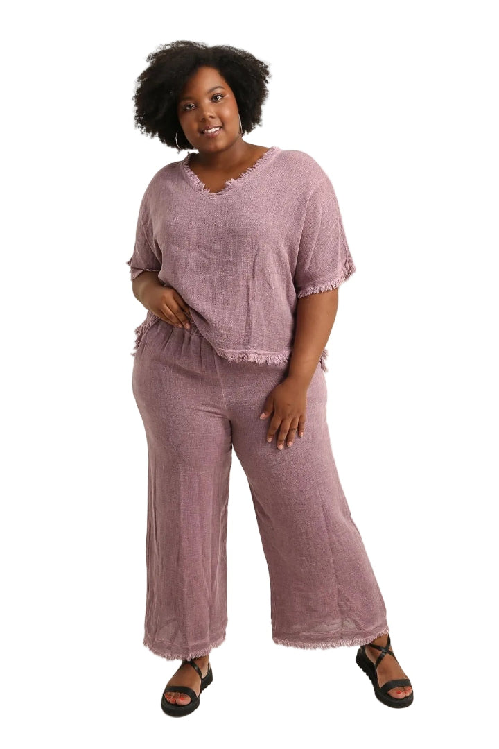 Woman wearing a bordeaux coloured outfit with wide-leg pants and sandals on a white background