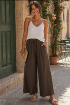 Woman wearing a white top and brown wide-leg pants standing in an outdoor setting.