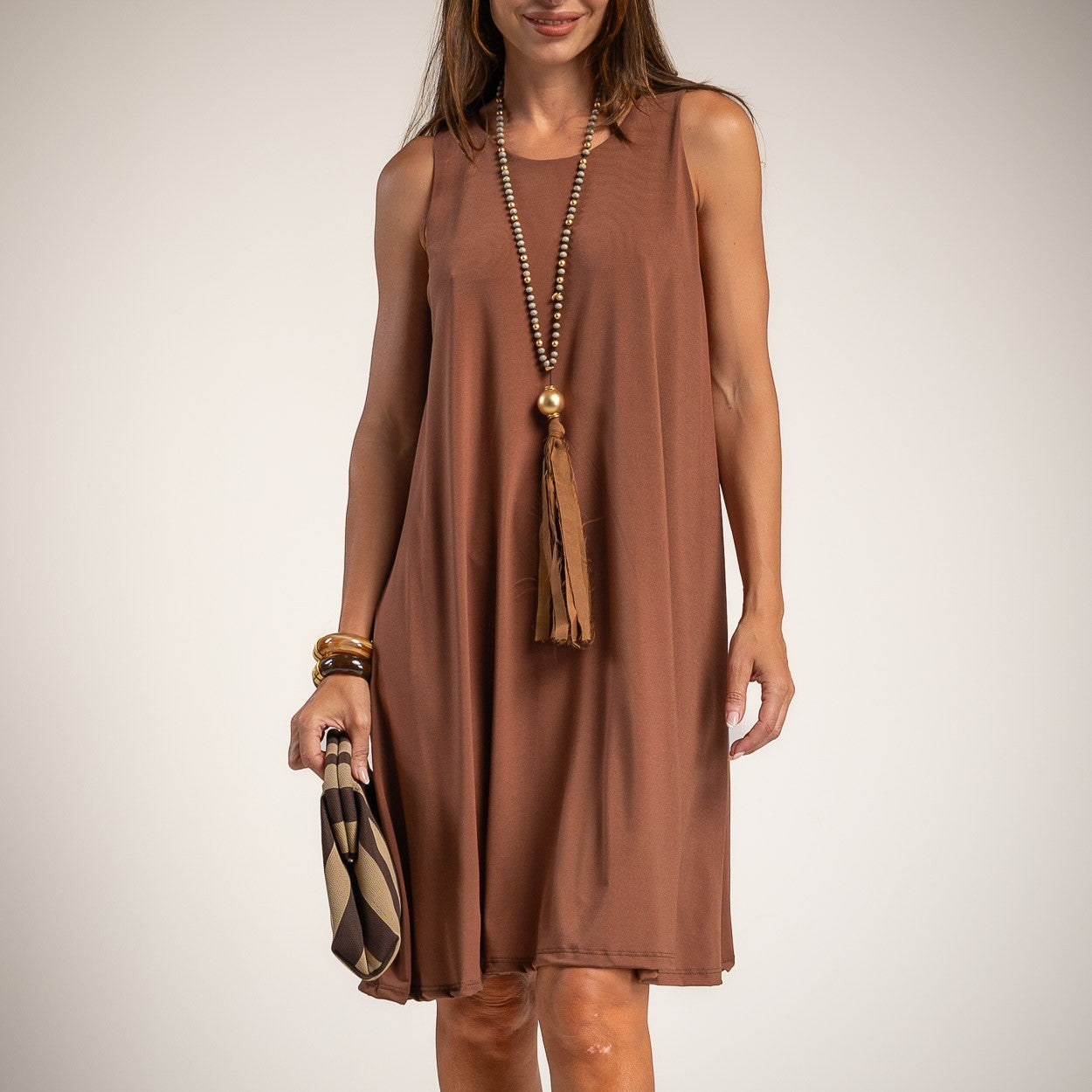 A woman wearing a sleeveless, knee-length brown dress with a relaxed A-line silhouette