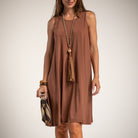 A woman wearing a sleeveless, knee-length brown dress with a relaxed A-line silhouette