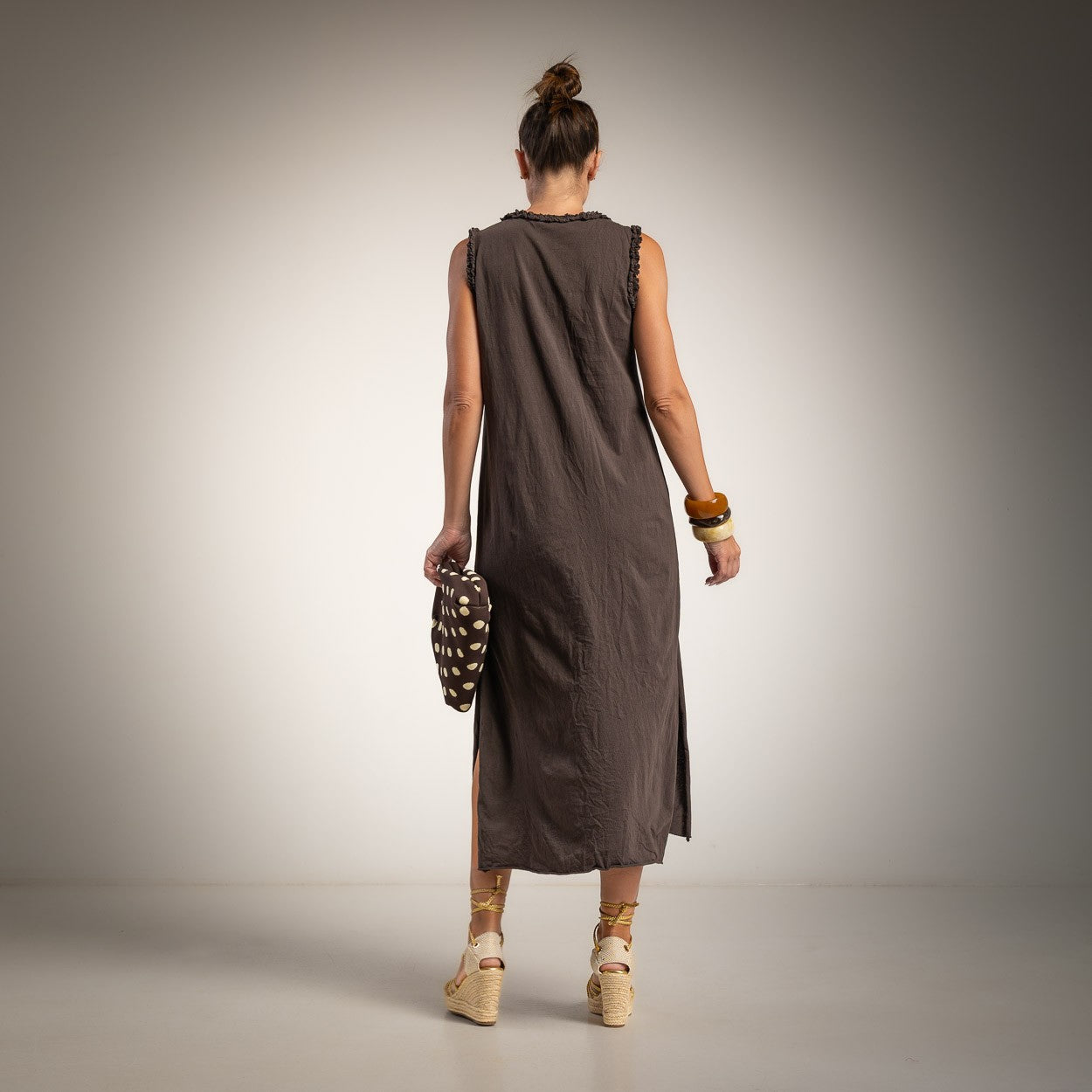 A woman is shown from behind wearing a sleeveless, dark brown linen midi dress with side slits