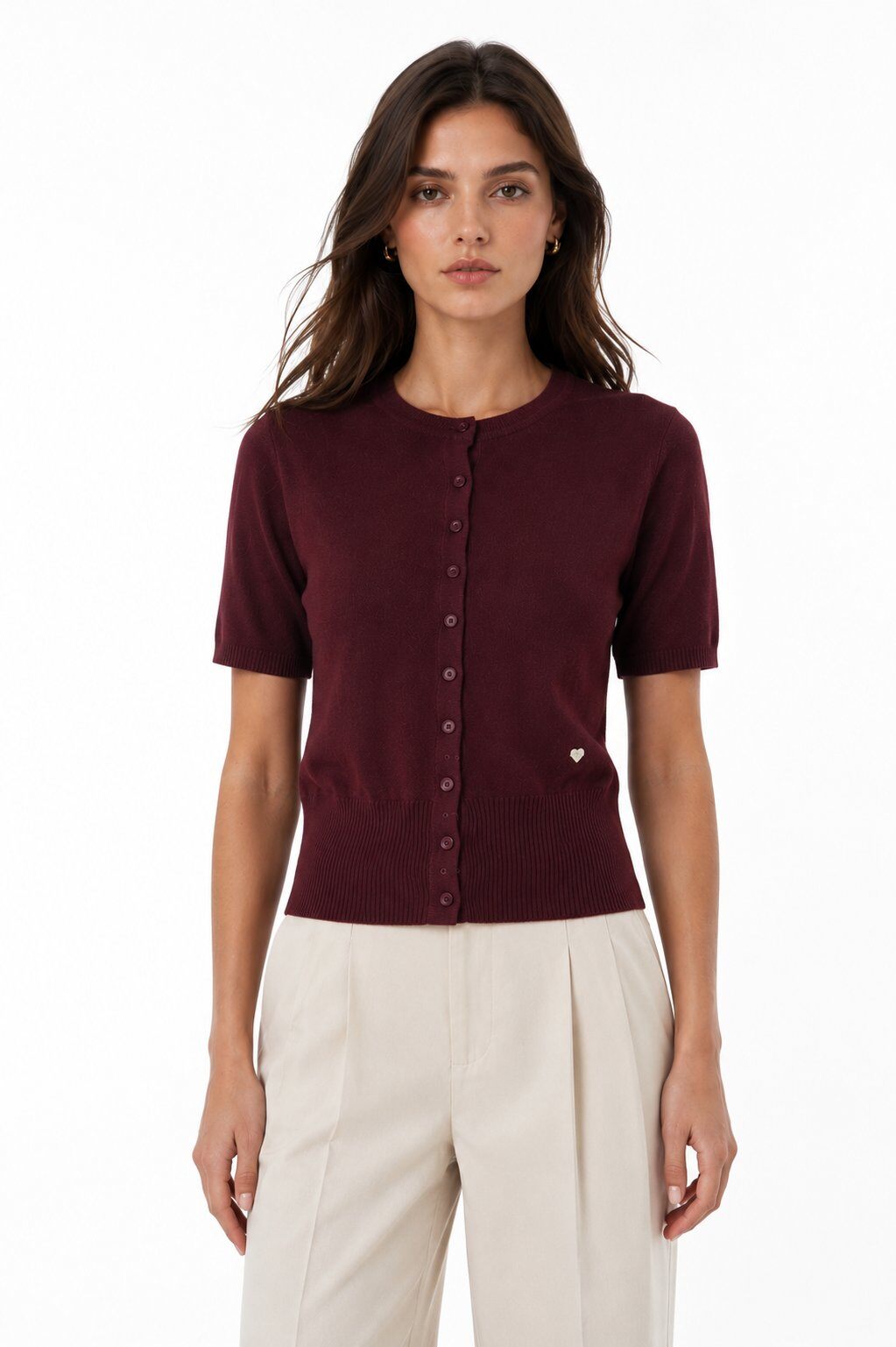 A woman modeling a short-sleeve burgundy knit top with a button-down front, paired with cream-colored trousers, against a plain white background.