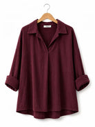 A dark burgundy long-sleeve shirt with a relaxed fit, a collar, and rolled cuffs, hanging on a wooden hanger against a plain white background.