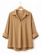A tan long-sleeve linen shirt with a collar and rolled cuffs, hanging on a wooden hanger against a white background.