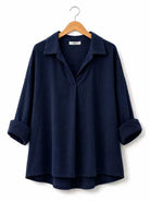 A dark navy blue long-sleeve collared shirt with rolled cuffs, hanging on a wooden hanger against a plain white background.