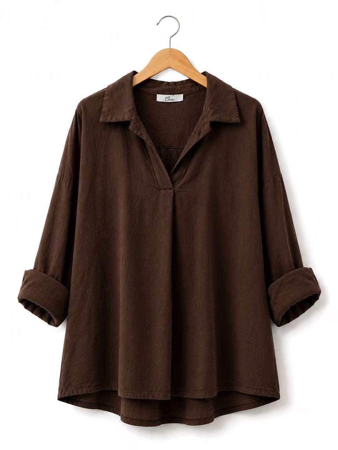 A dark brown long-sleeve collared shirt with rolled cuffs and a split V-neckline, hanging on a wooden hanger against a plain white background.