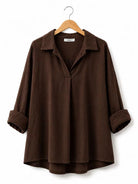 A dark brown long-sleeve collared shirt with rolled cuffs and a split V-neckline, hanging on a wooden hanger against a plain white background.