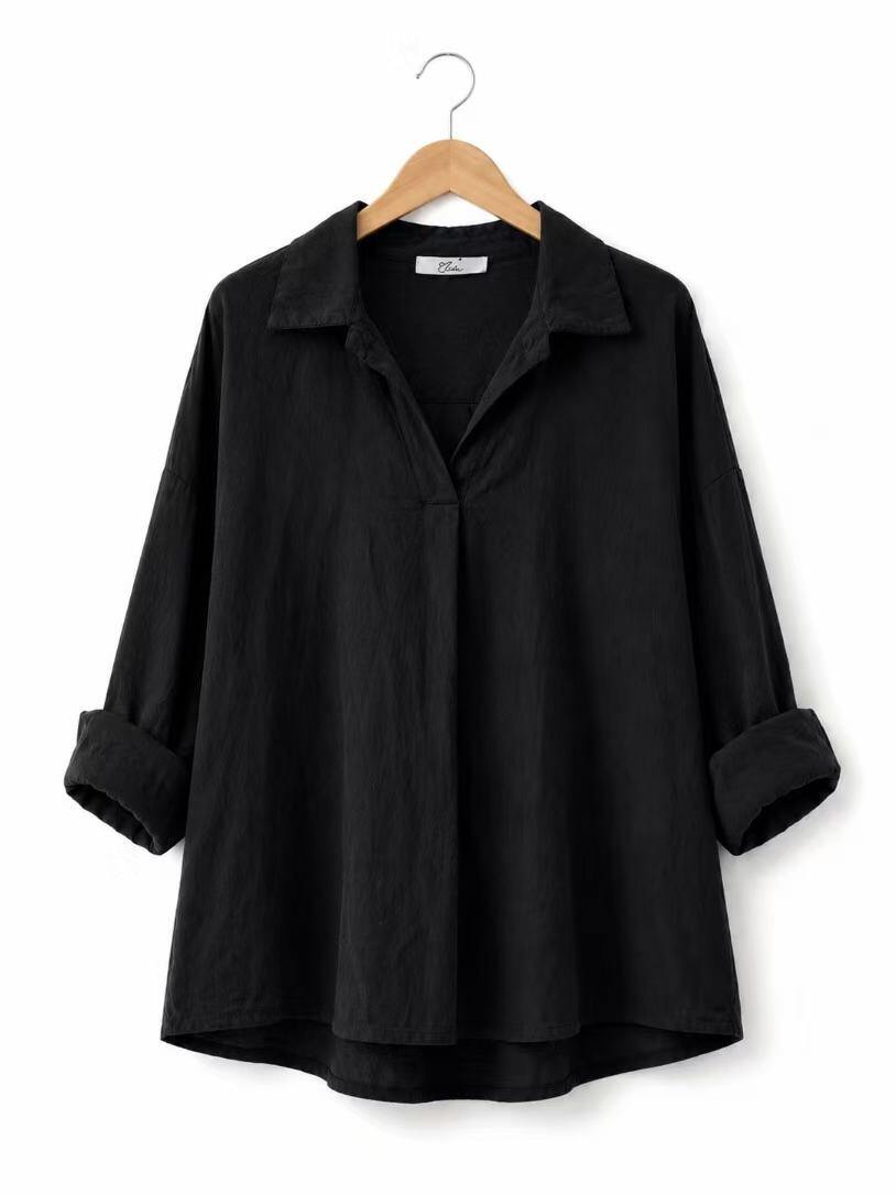 A black long-sleeve shirt with a relaxed, oversized fit, displayed on a wooden hanger against a plain white background.